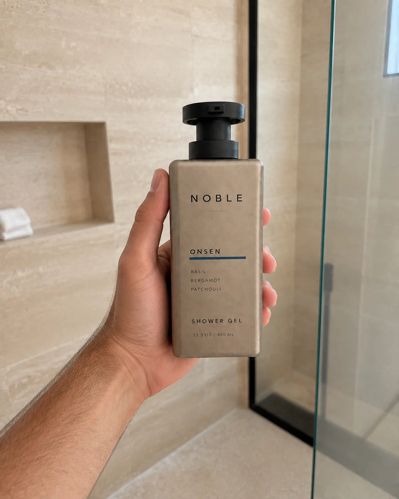 A hand holds the ONSEN 13.5 oz metal bottle in a light stone shower