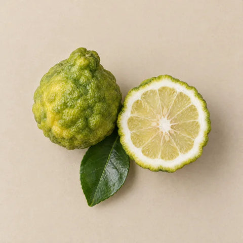 A whole bergamot, a halved bergamot and a citrus leaf on pale stone