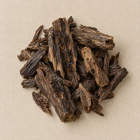 Dark resin-streaked oud wood chips on pale stone